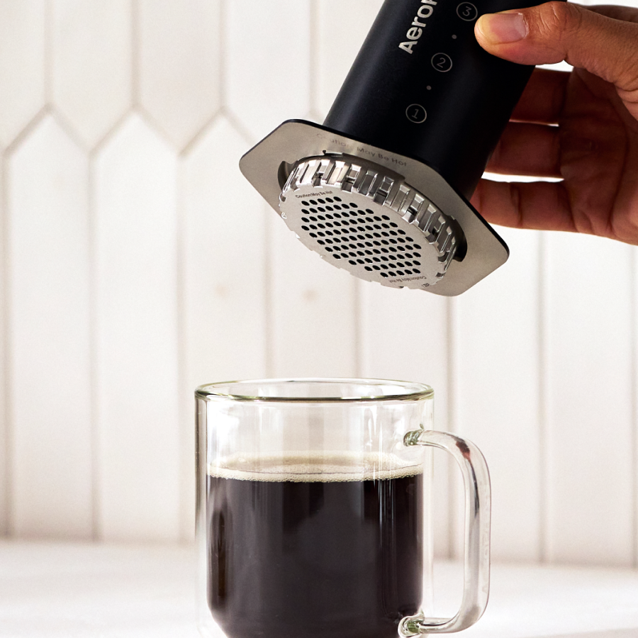 Hand pressing coffee with a black Aeropress Steel into a glass