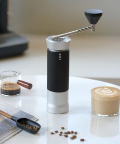 Silver Millab M01 hand grinder next to an espresso and a latte